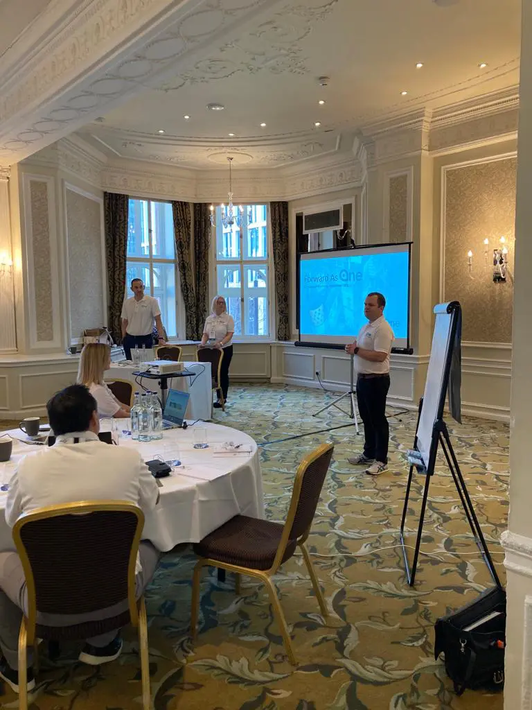 Three people at Global Partner Day 2023 in a conference room with screen and flipchart.