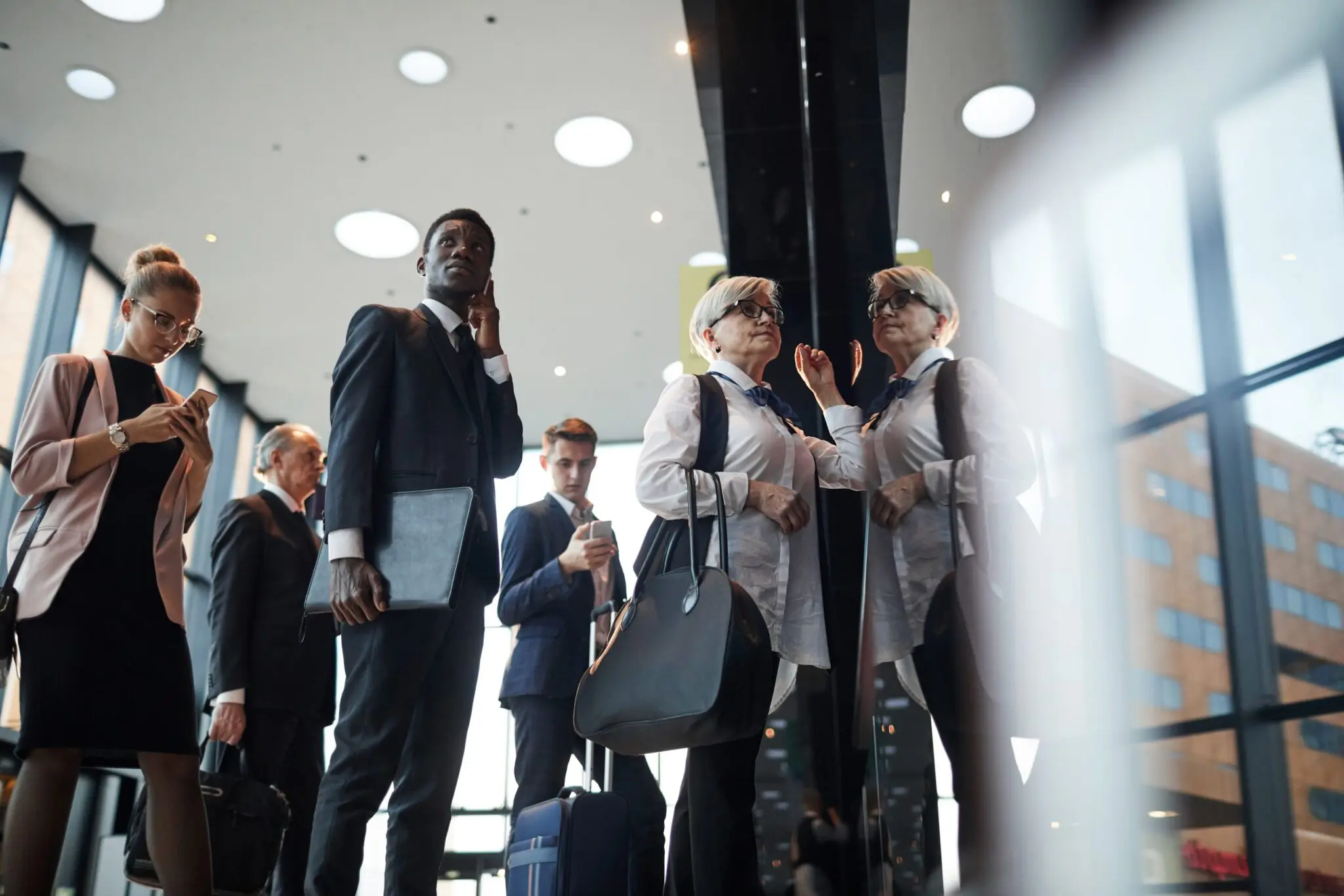 Businesspeople with luggage stand inside a busy airport.