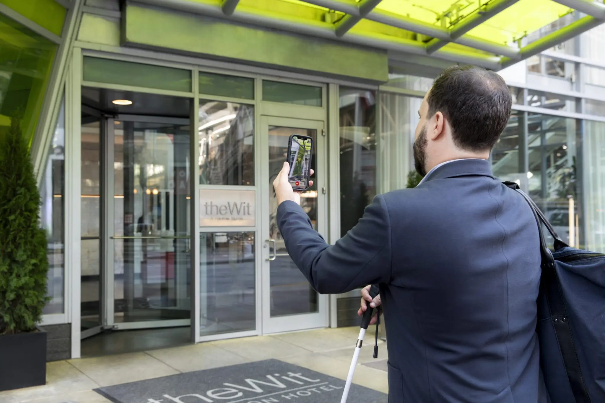 Man with walking stick using mobile outside theWit Hotel entrance.