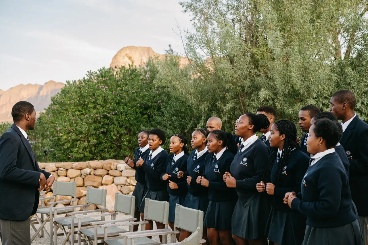 Students in uniforms stand outside with a choir instructor at a conference.