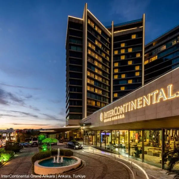 IHG hotel exterior with lit signage, glass windows, and fountain at dusk for business travellers.