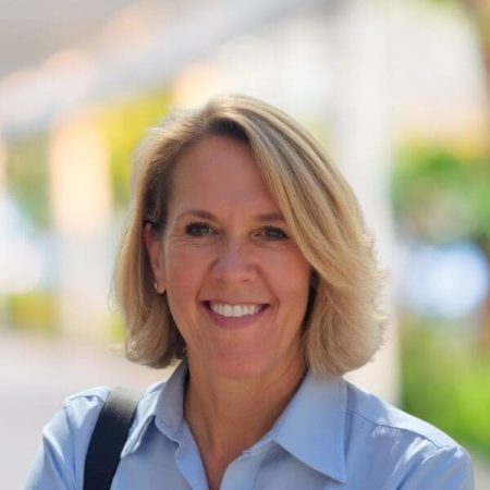 Smiling blonde woman outdoors in a blue shirt with a bag.