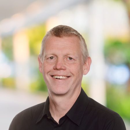 Smiling man with short fair hair in black shirt outdoors.